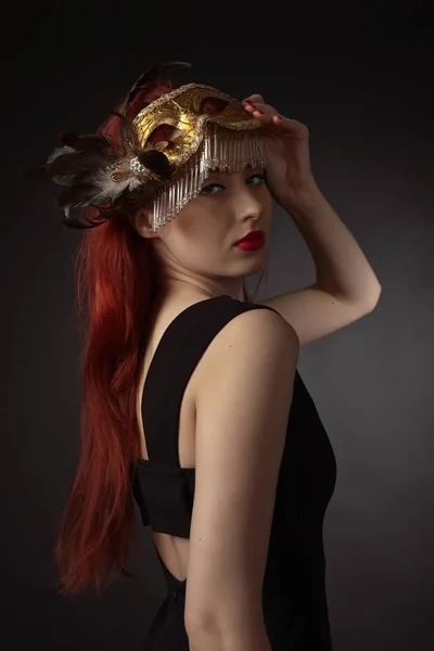 Belle femme rousse avec masque de carnaval sur fond noir — Photo