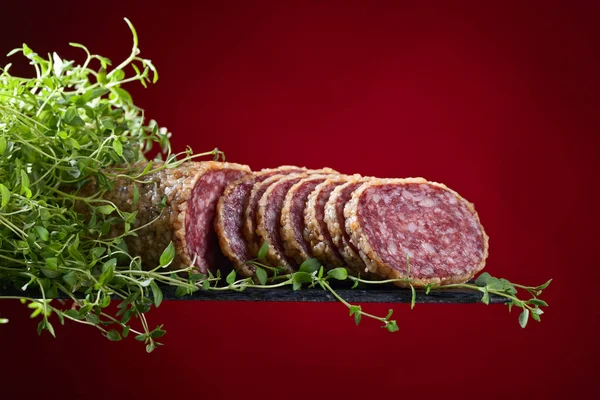 Нарізані салямі з чебрецем на червоному тлі — стокове фото
