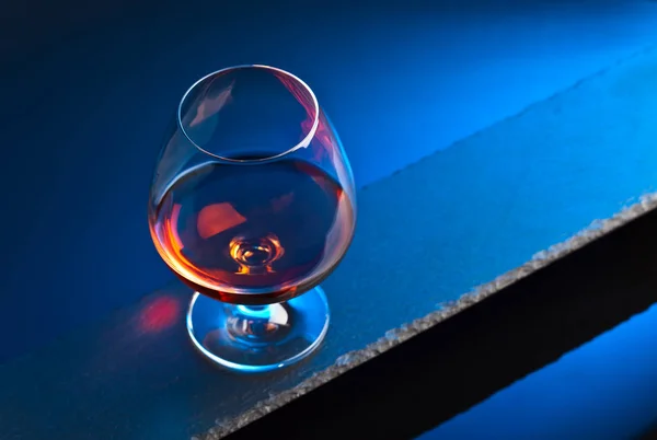 Glas mit Brandy auf blauem Hintergrund — Stockfoto