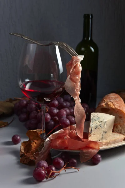 Jamon, queijo, uva e vinho tinto na mesa da cozinha — Fotografia de Stock