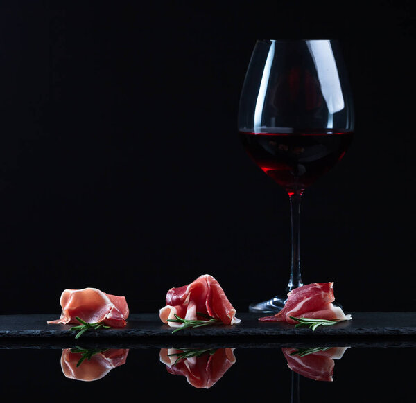 jamon with rosemary and glass of red wine on a black background