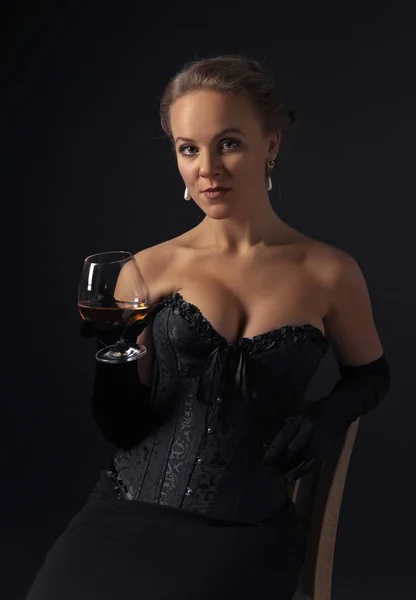 Ung vacker kvinna i svart korsett med glas konjak — Stockfoto