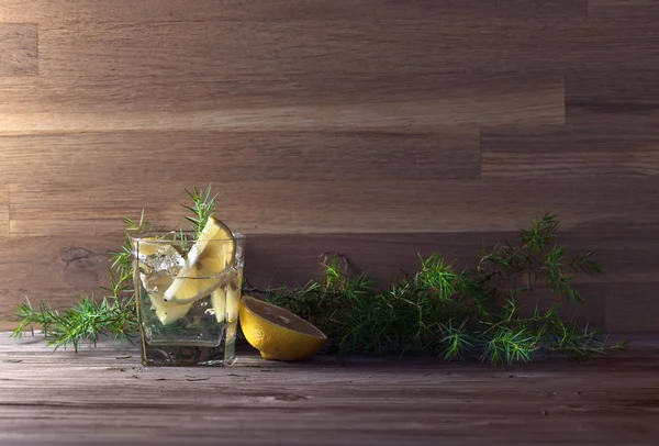Джин с лимоном, льдом и можжевеловой веткой на старом деревянном столе — стоковое фото