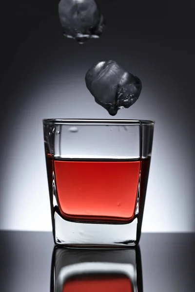 Un vaso de whisky con hielo cayendo sobre un fondo negro —  Fotos de Stock