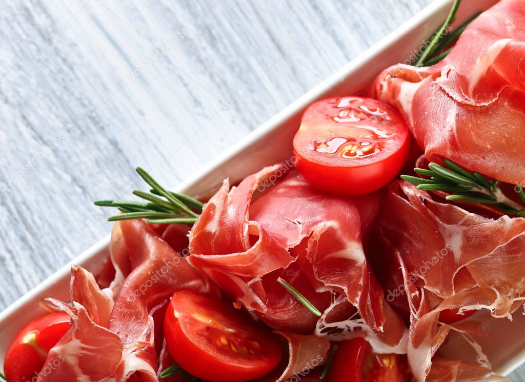  Prosciutto with  rosemary and tomato on a wooden table