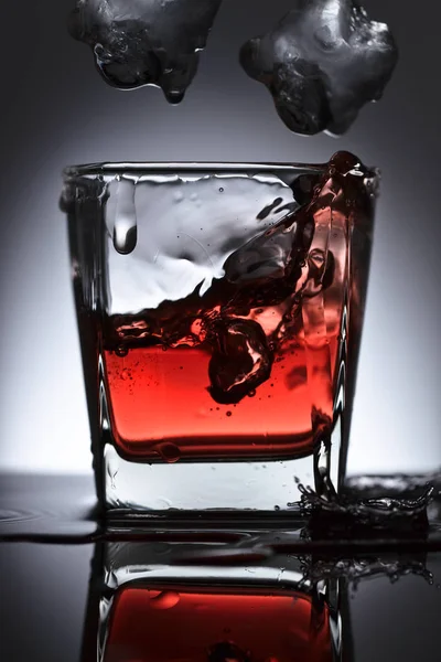 Glass of whiskey with falling ice on a black background — Stock Photo, Image