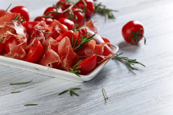 Prosciutto com alecrim e tomate em uma mesa de madeira — Fotografia de Stock