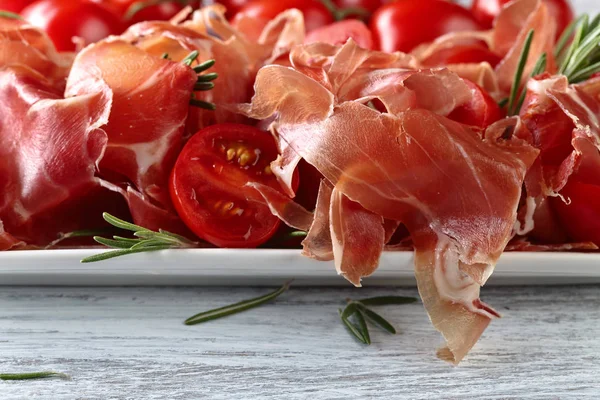 Prosciutto com alecrim e tomate em uma mesa de madeira — Fotografia de Stock