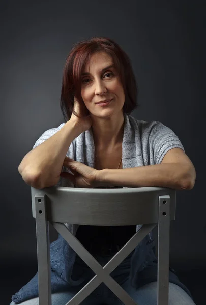 Portrait of middle aged woman on a gray chair — Stock Photo, Image