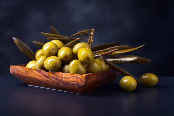 Olive verdi in un piatto di legno su un tavolo nero — Foto Stock