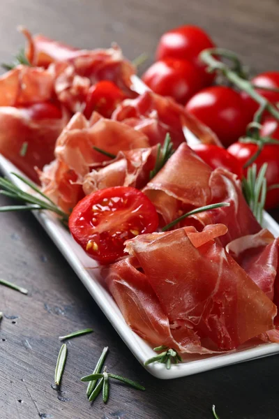 Prosciutto with  rosemary and tomato on a wooden table — Stock Photo, Image