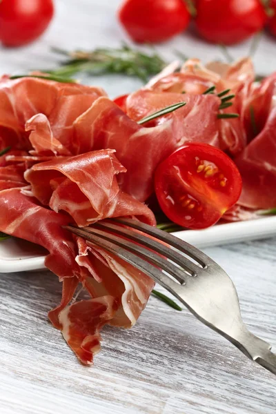 Prosciutto com alecrim e tomate em uma mesa de madeira — Fotografia de Stock