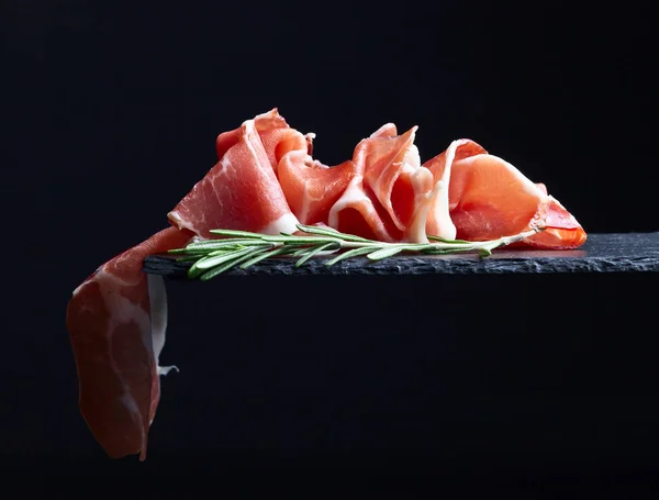 Prosciutto con rosmarino su fondo nero — Foto Stock