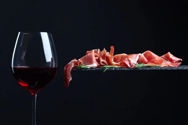 Prosciutto with rosemary and red wine on a black  background — Stock Photo, Image
