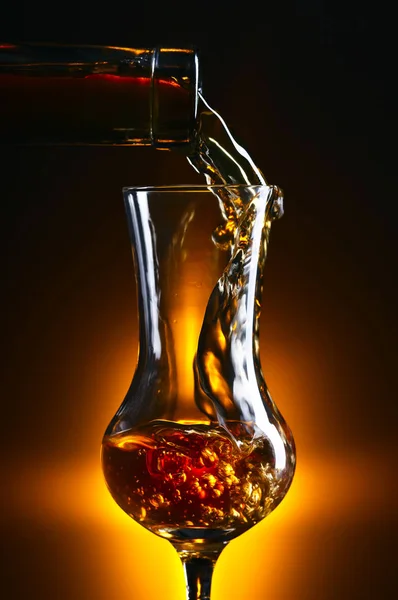 Pouring alcohol into a glass on dark background — Stock Photo, Image