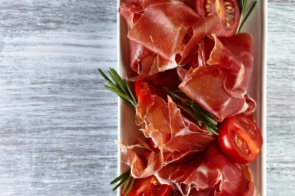 Prosciutto with  rosemary and tomato on a wooden table, free sp — Stock Photo, Image