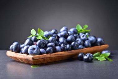 Ahşap tabak içinde yeşil şubesi ile taze sulu yaban mersini 