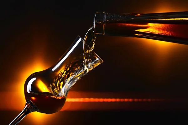 Pouring alcoholic drink into a glass on dark background — Stock Photo, Image