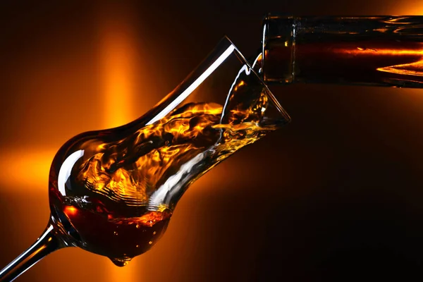 Pouring alcoholic drink into a glass on dark background