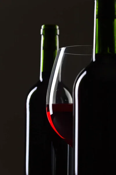 Flaschen und ein Glas Rotwein auf schwarzem Hintergrund . — Stockfoto