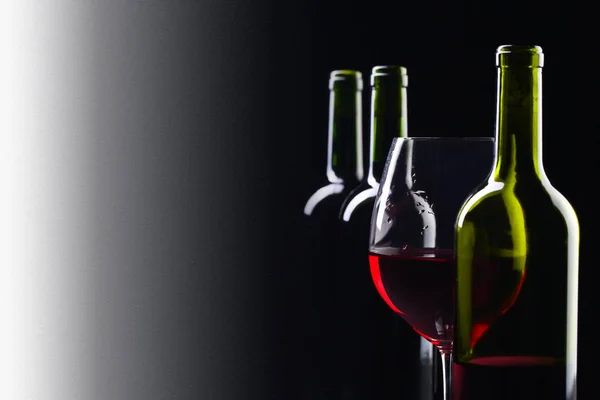 Μπουκάλια και ποτήρι κόκκινο κρασί πάνω σε μαύρο φόντο . — Φωτογραφία Αρχείου