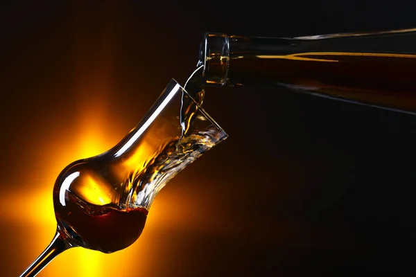 Wylewanie alkoholu w szklance na ciemnym tle — Zdjęcie stockowe