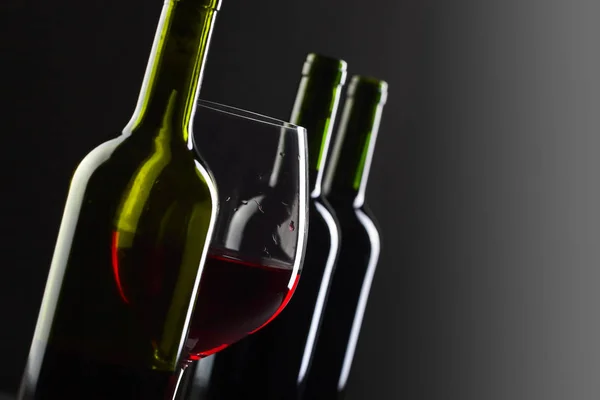 Bouteilles et verre de vin rouge sur fond noir  . — Photo