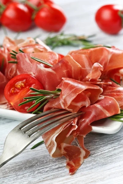 Prosciutto with  rosemary and tomato on a wooden table — Stock Photo, Image