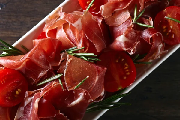 Prosciutto with  rosemary and tomato on a wooden table — Stock Photo, Image