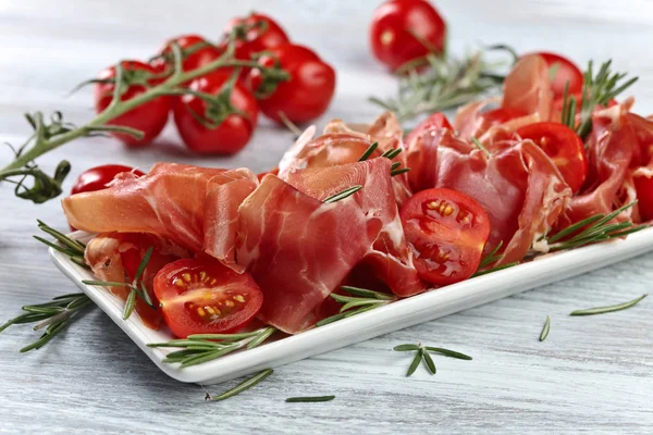 Prosciutto com alecrim e tomate em uma mesa de madeira — Fotografia de Stock