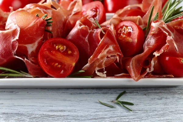 Prosciutto com alecrim e tomate em uma mesa de madeira — Fotografia de Stock