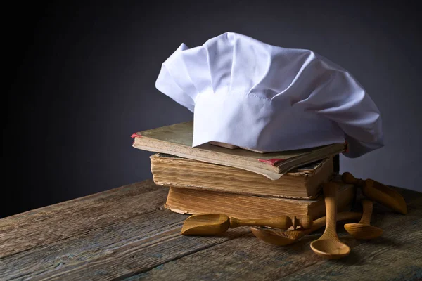 Old culinary books , chef hat and wooden spoons .