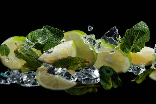 Lime pieces with leaves of peppermint on black background. — Stock Photo, Image