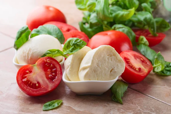 Mozzarella cheese with tomatoes and green basil on a kitchen ta — Stock Photo, Image