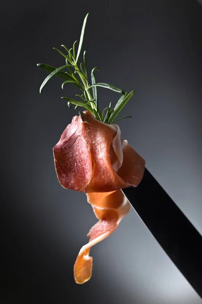Prosciutto med rosmarin på ett knivblad. — Stockfoto