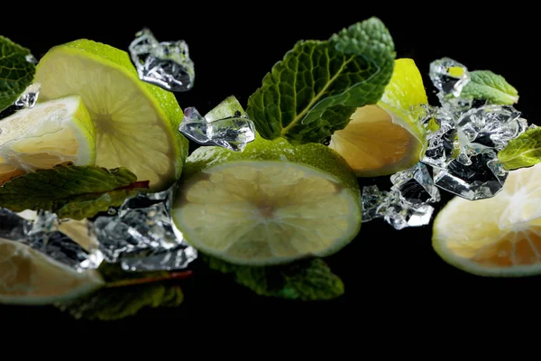 Lime pieces with leaves of peppermint on black background. — Stock Photo, Image