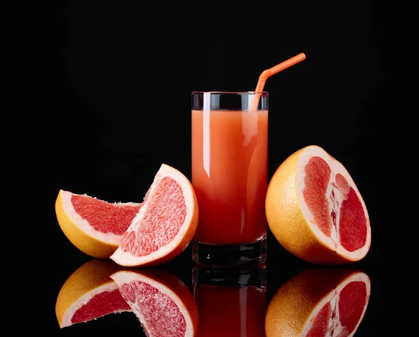 Glas Grapefruitsaft und geschnittene Früchte auf schwarzem Hintergrund. — Stockfoto