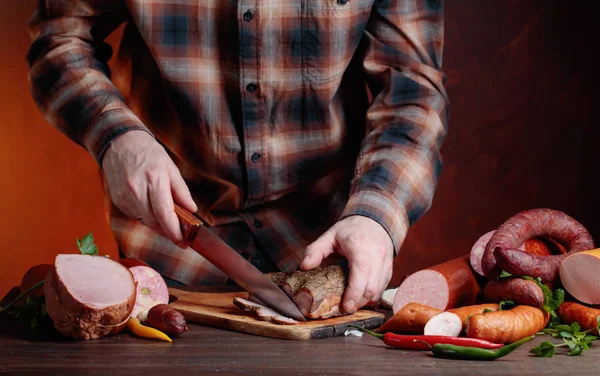 Homem corta várias salsichas e carne defumada  . — Fotografia de Stock