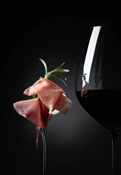 Glass of red wine with prosciutto and rosemary. — Stock Photo, Image