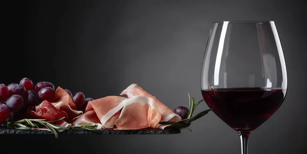 Prosciutto with rosemary and glass of red wine. — Stock Photo, Image