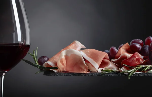 Prosciutto met rozemarijn en glas rode wijn. — Stockfoto