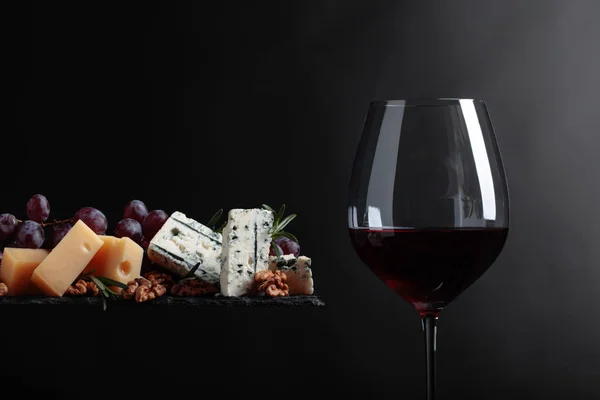 Glas rode wijn met diverse kazen, druiven en walnoten . — Stockfoto