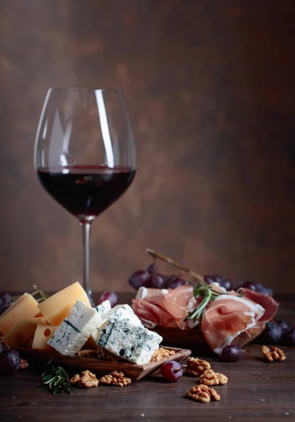 Çeşitli peynirler, meyve ve prosciutto ile kırmızı şarap . — Stok fotoğraf