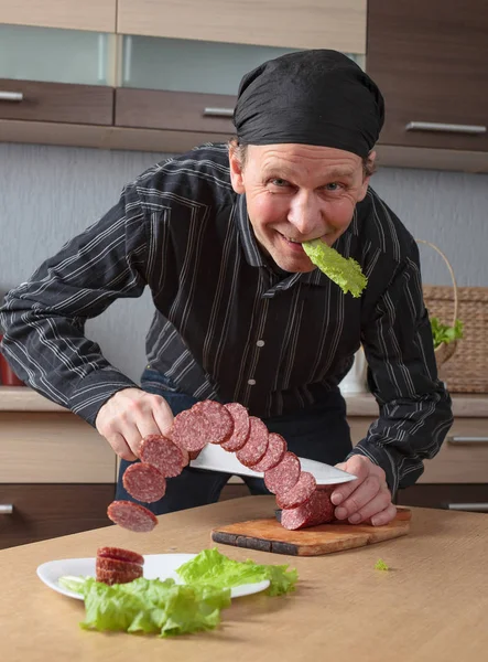 Man met een mes snijdt stukken worst. — Stockfoto