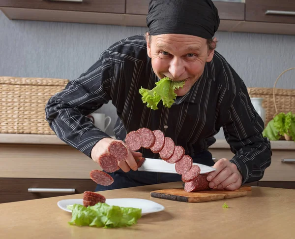 Homem com uma faca corta pedaços de salsicha . — Fotografia de Stock