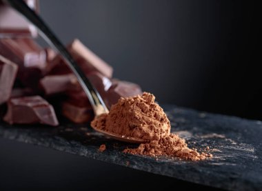 Kırık çikolata parçaları ve siyah arka plan üzerine kakao tozu.