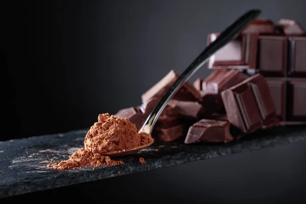 Разбитые кусочки шоколада и какао порошок на черном фоне . — стоковое фото