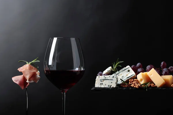 Copa de vino tinto con varios quesos, uvas y jamón  . — Foto de Stock