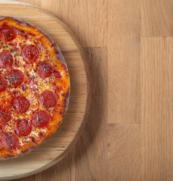 Färsk backas pizza med salami på en träskiva. — Stockfoto