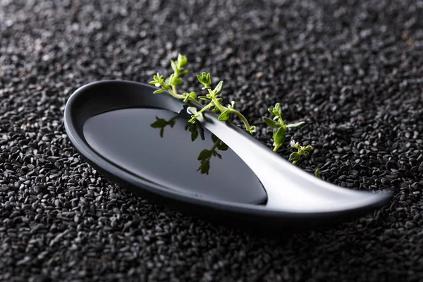 Plant oil  with thyme branches on a background of black sesame. — Stock Photo, Image